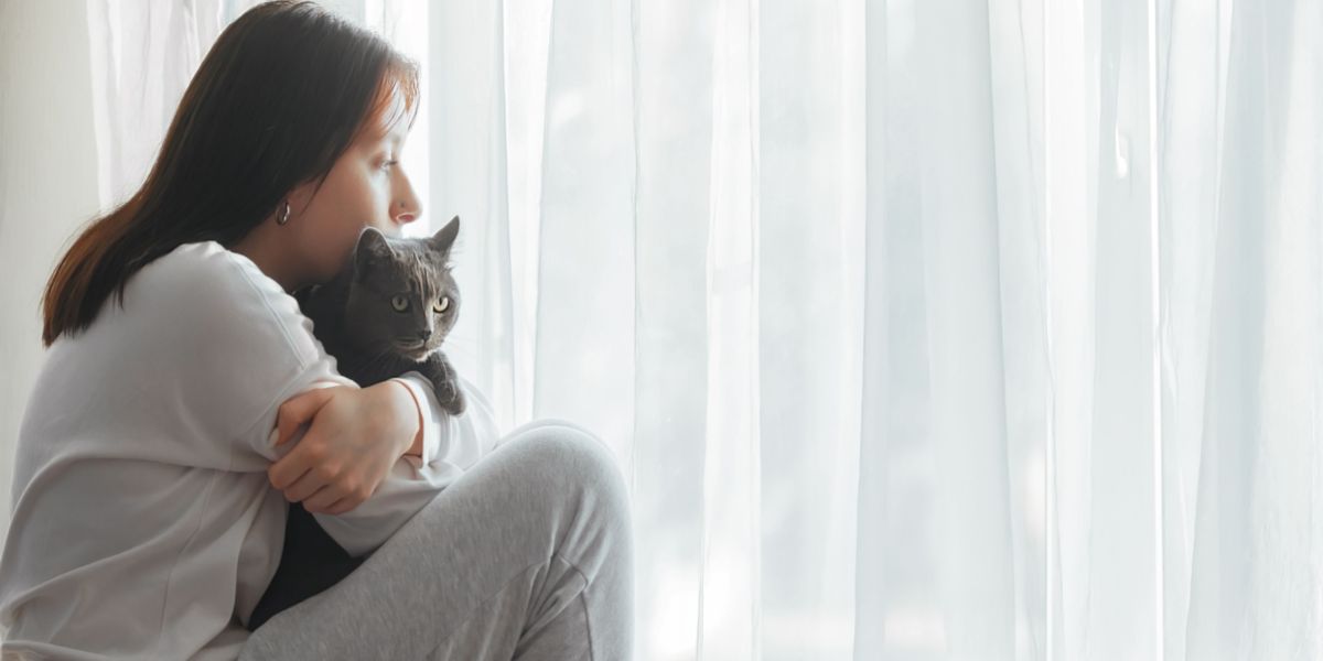 Bild einer Frau, die traurig aussieht, während sie mit einer Katze zusammensitzt, was möglicherweise auf einen Moment des Trostes oder der Unterstützung hindeutet.