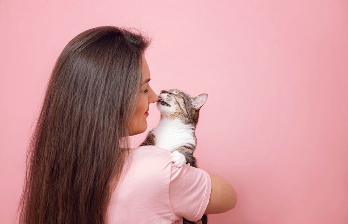 Das Bild zeigt eine süße Interaktion, bei der eine neugierige Katze zärtlich die Hand eines erfreuten Mädchens leckt und so die Bindung zwischen den beiden hervorhebt.